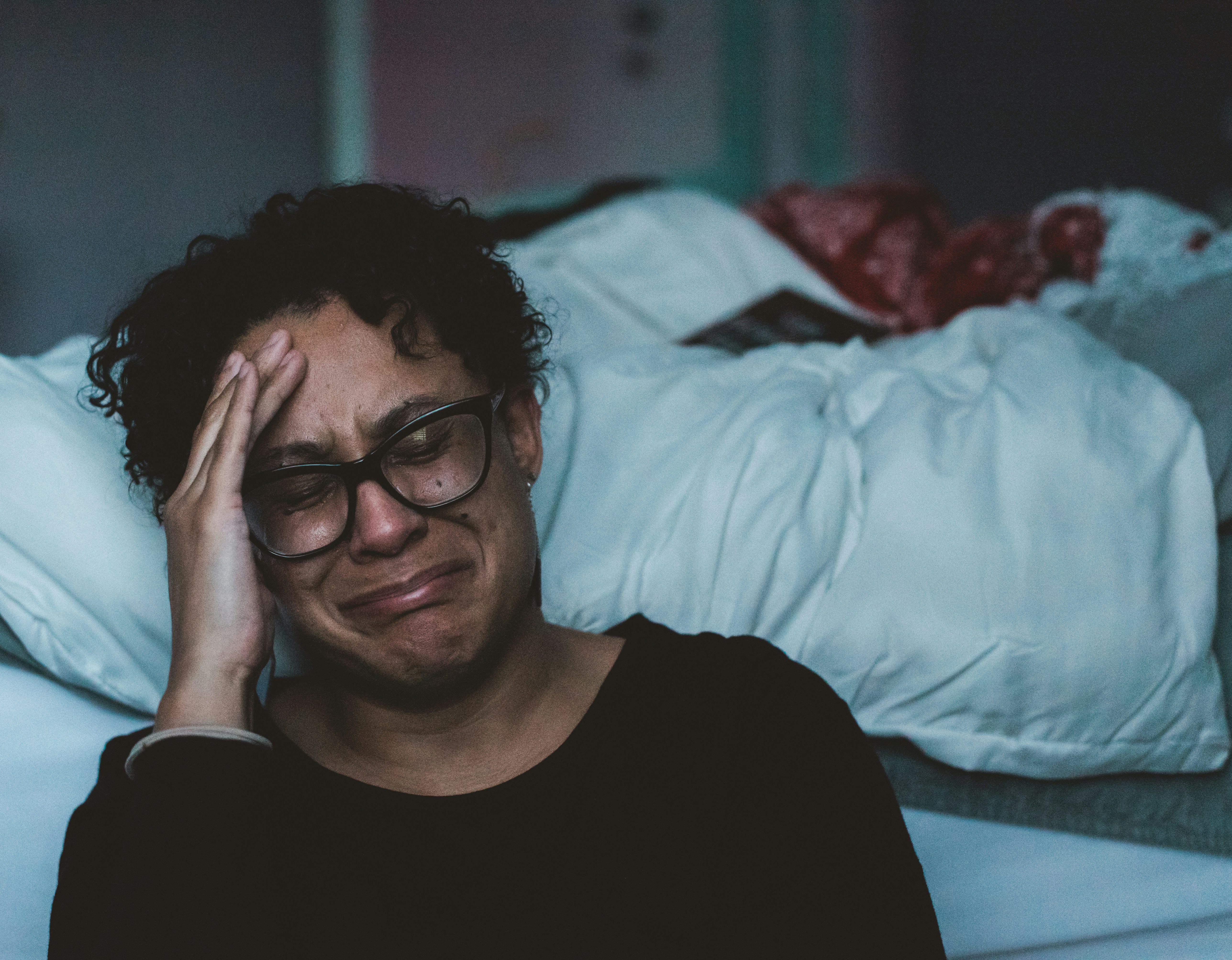 woman sitting on the side of the bed. wearing a black shirt, holding her head, and crying